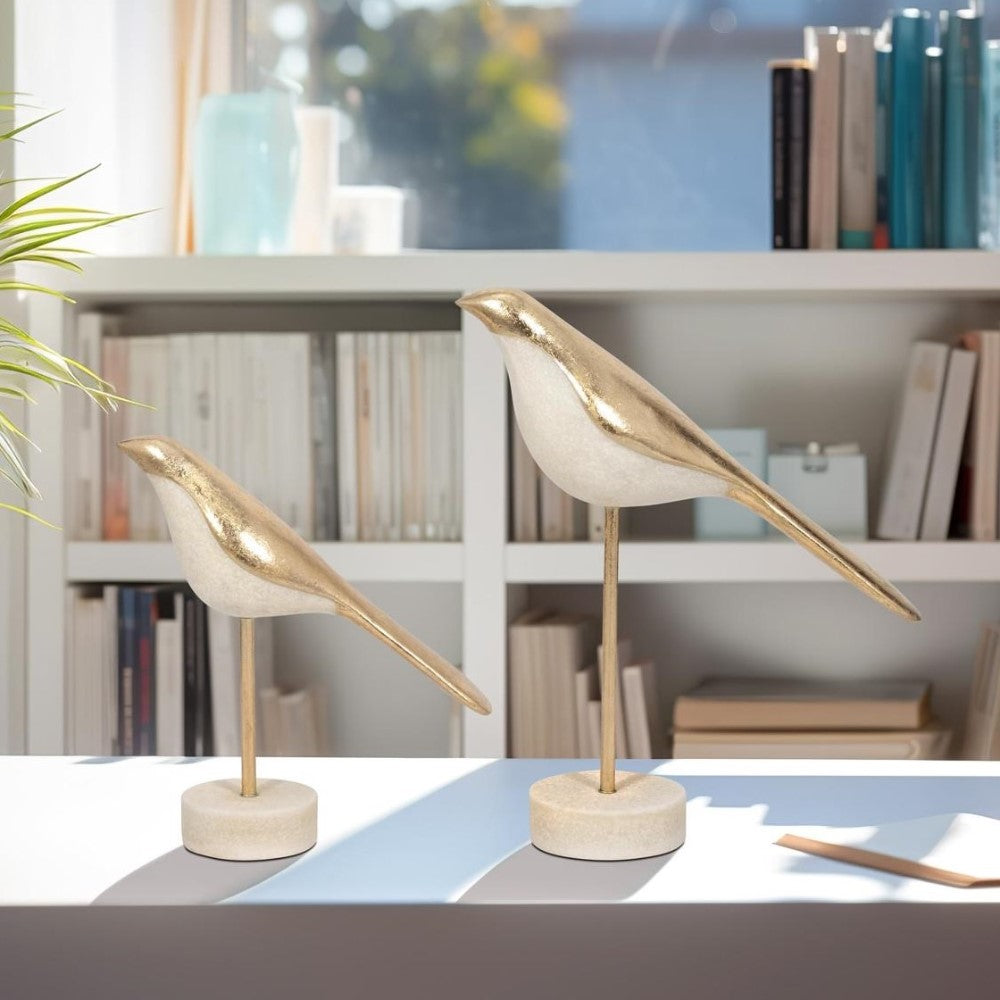 Gold bird sculptures on stands in a bright, bookshelf-filled room.