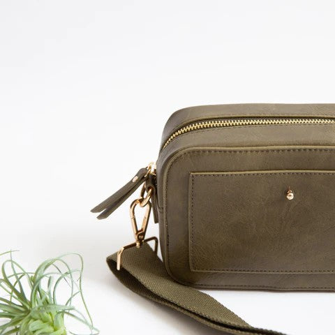 Olive green leather bag with a strap next to a small plant.