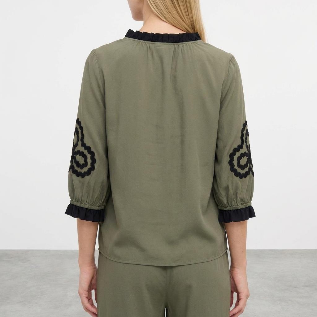 Woman in green blouse with black embroidery stands facing away.