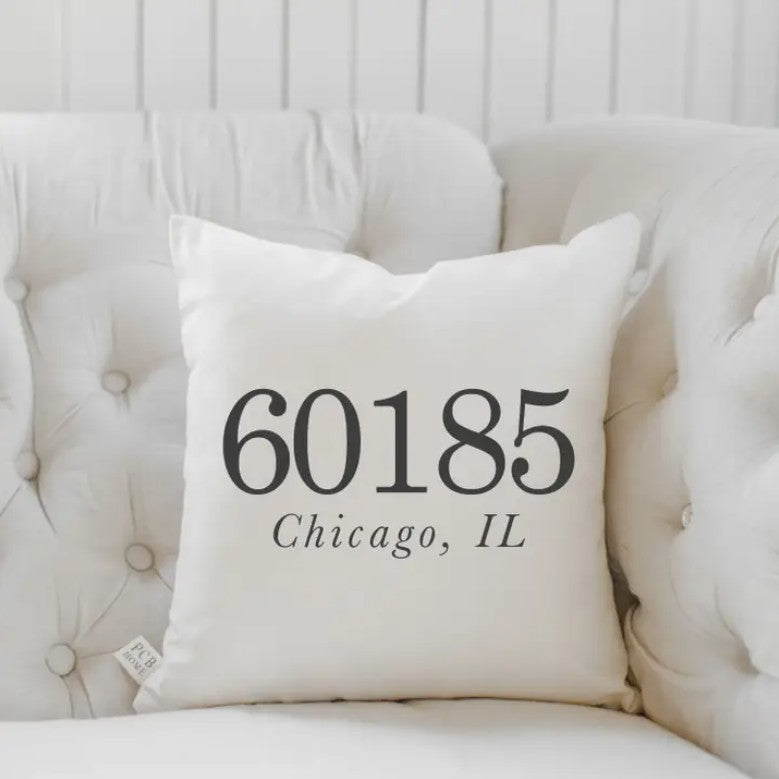 White pillow with "60185, Chicago, IL" on a tufted sofa.