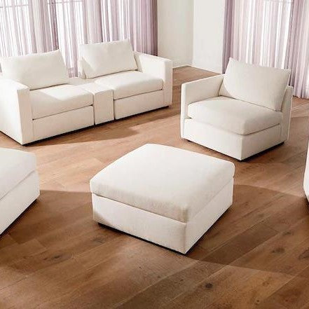 Modern white sofas and an ottoman on wooden flooring with sheer curtains.