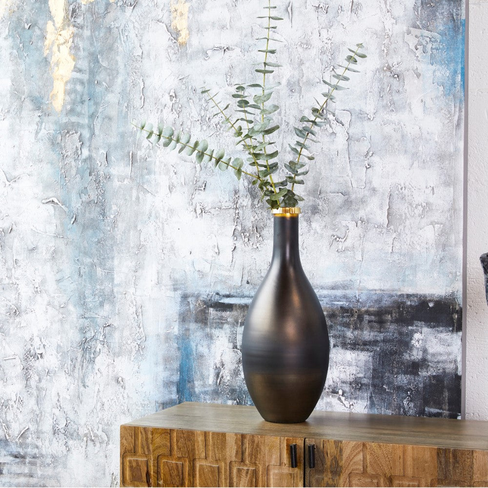 Tall vase with greenery on a wooden table, abstract blue artwork behind.