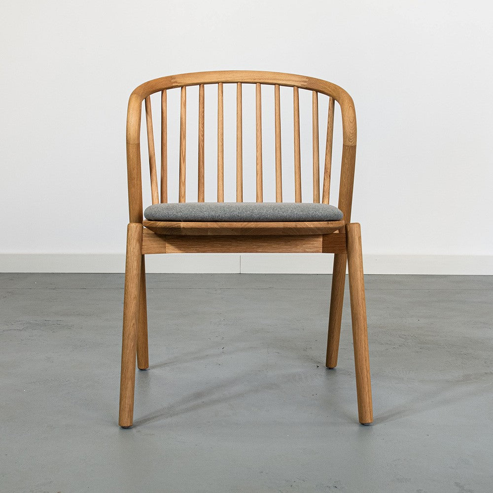 Wooden chair with a gray cushion on a concrete floor.