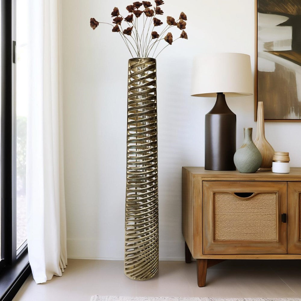Tall spiral vase with dried flowers next to a wooden cabinet and table lamp.