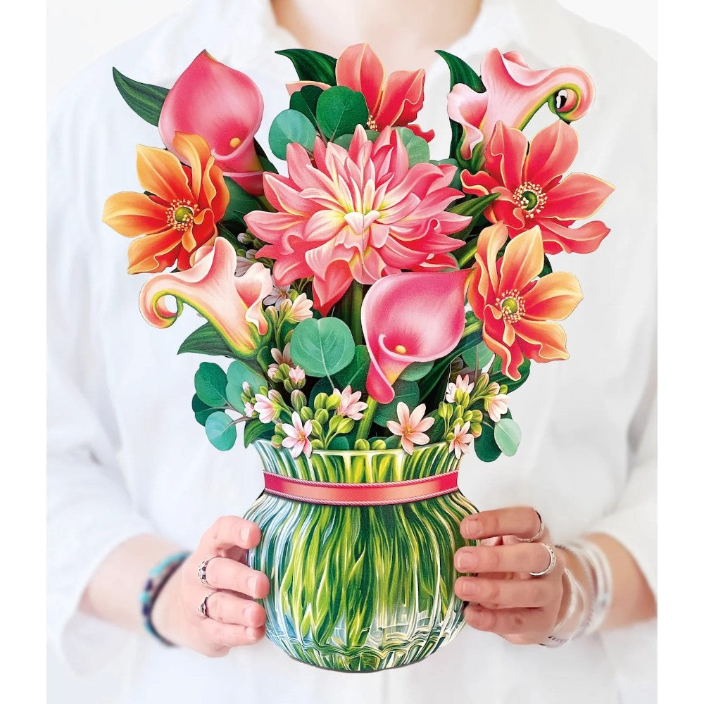 Person holding a vase of colorful flowers in a white shirt.