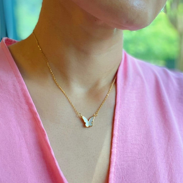 Gold butterfly necklace on person in pink top.