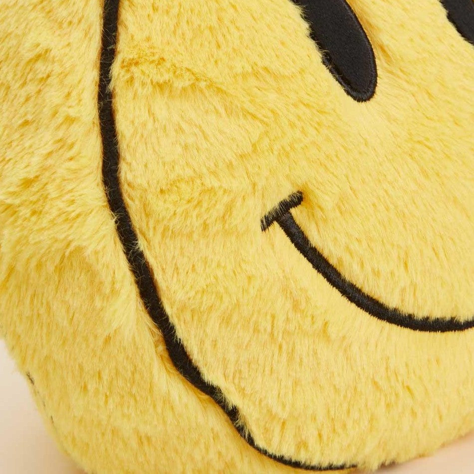 Close-up of a furry yellow smiley face pillow.