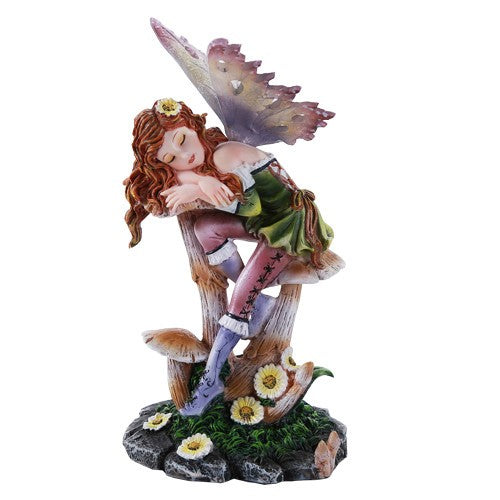 Fairy figurine resting on mushrooms with flowers around, wearing green dress and colorful wings.