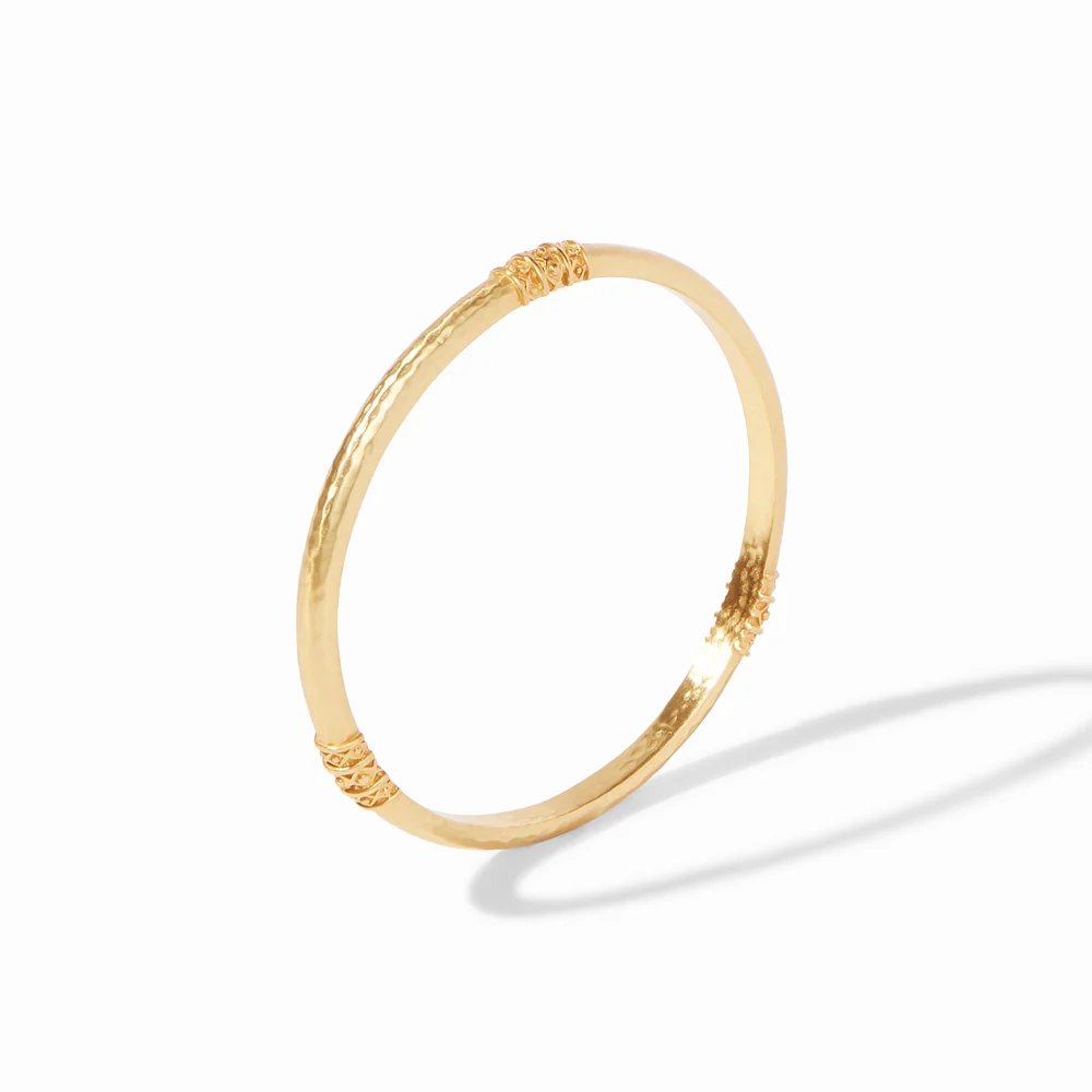 A delicate gold bangle with ornate textured accents, photographed against a white background.