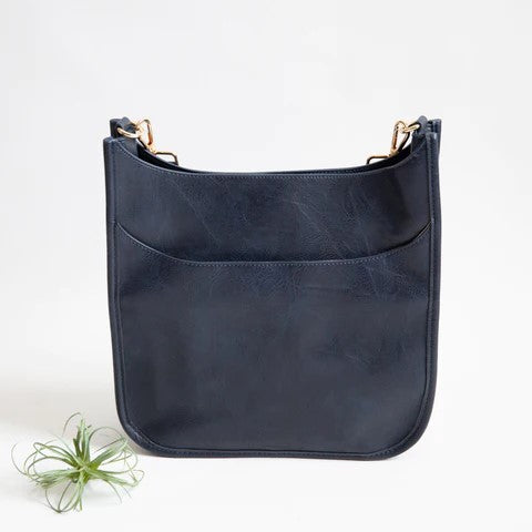 Navy leather bag with gold accents next to a small plant on a white background.
