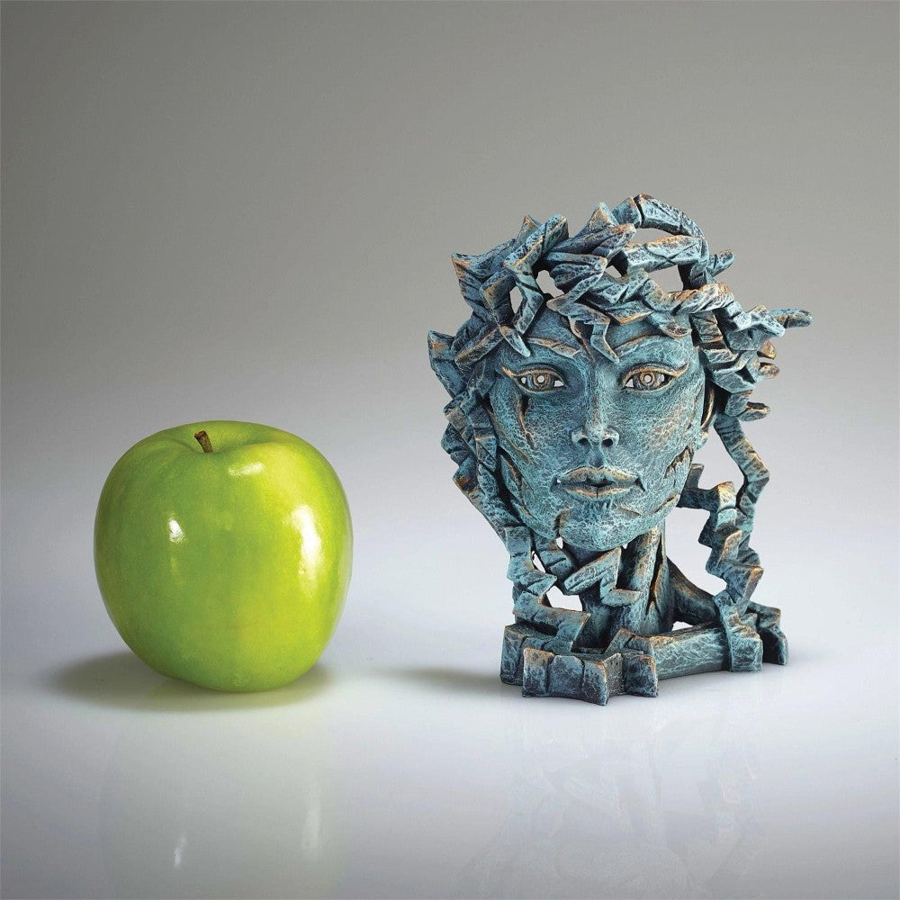 Green apple beside a textured, blue stone sculpture of a face on a reflective surface.