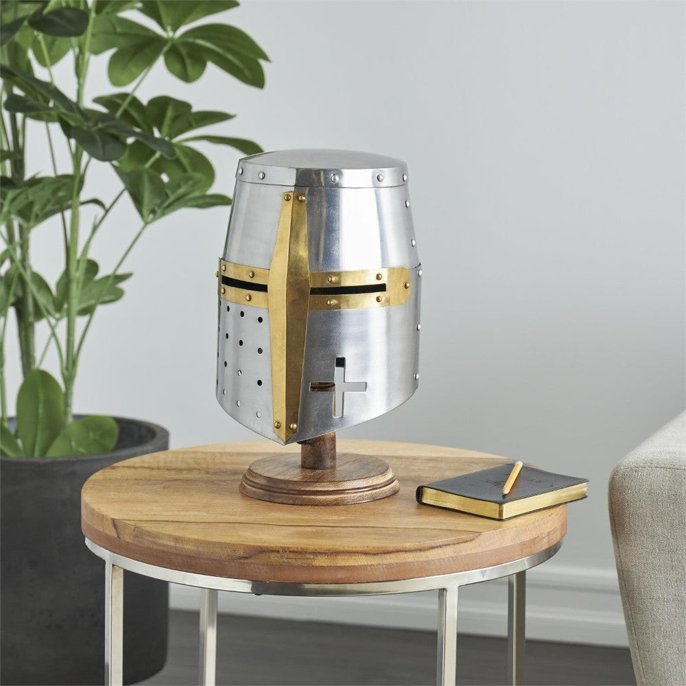 Medieval helmet on a wooden table beside a plant and a notebook.