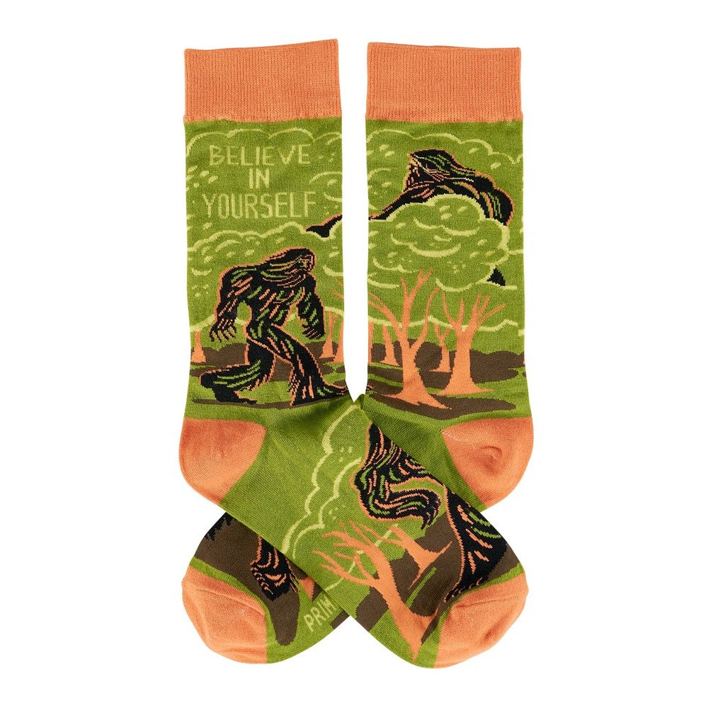 Green and orange socks with Bigfoot and "Believe in Yourself" text.