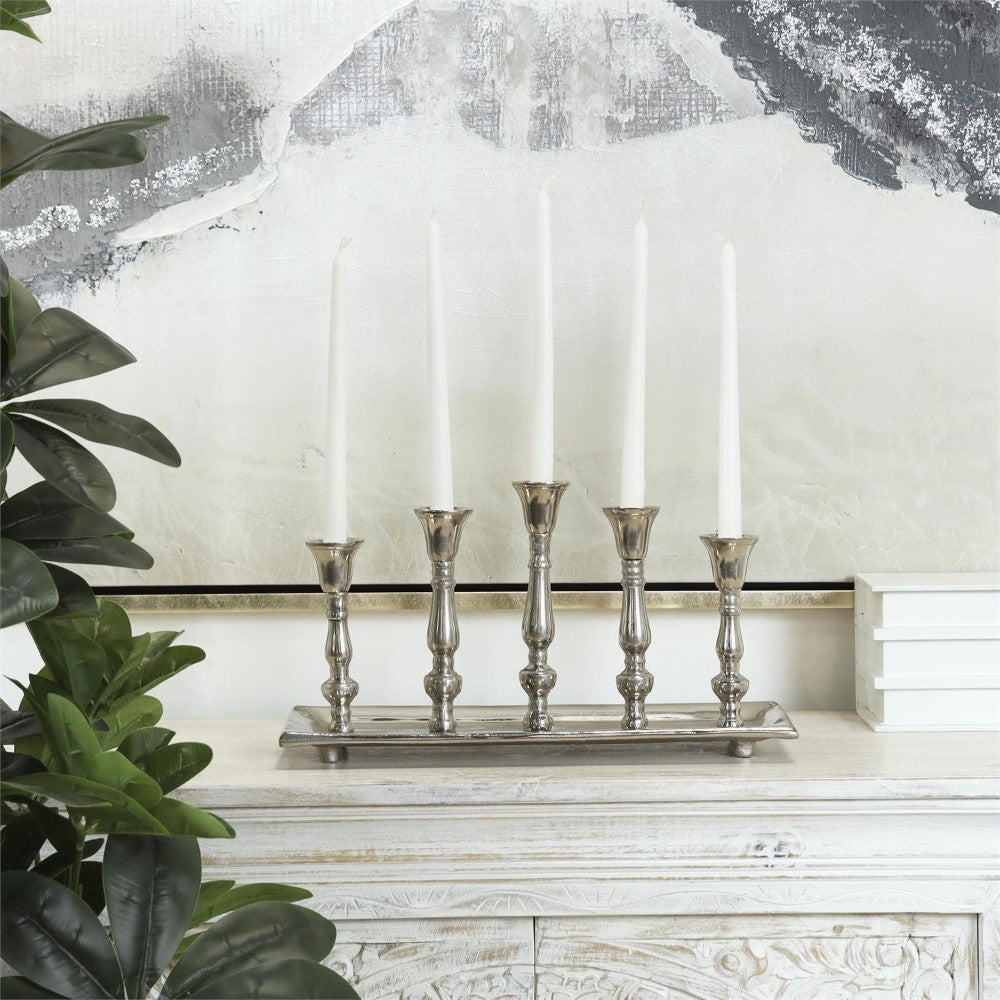 Ornate silver candlesticks with white candles on a wooden mantel.