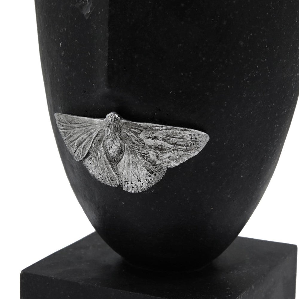 Silver moth on black stone vase, close-up view.