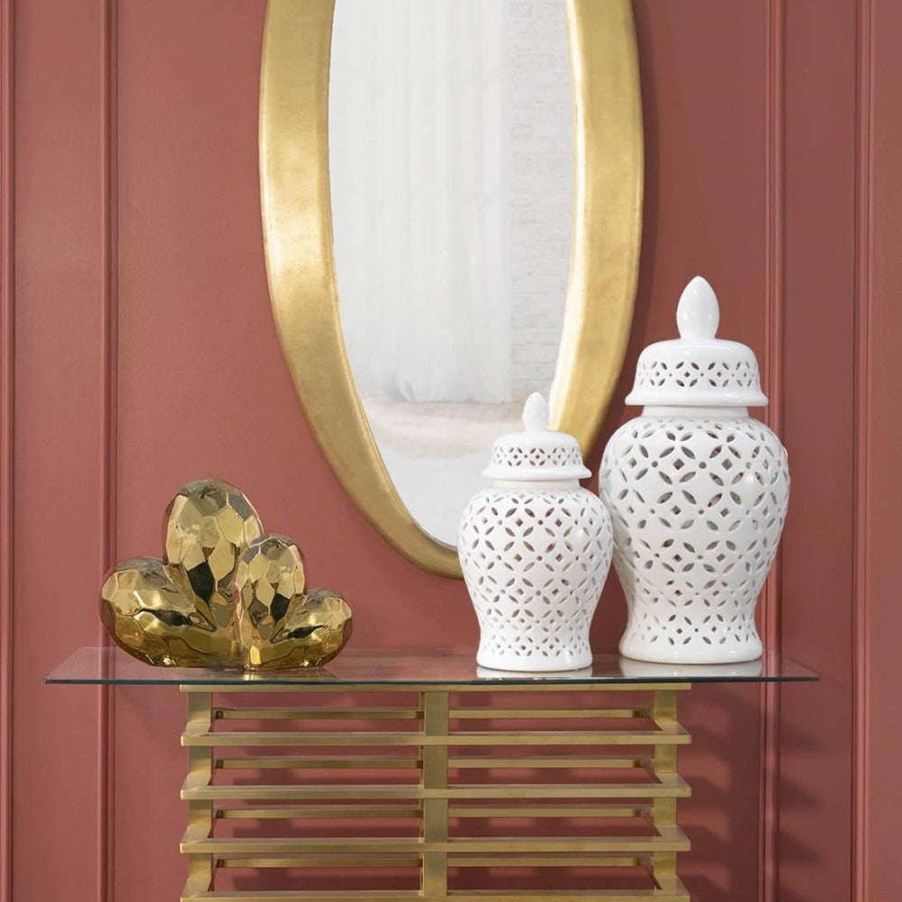Oval mirror and ornate vases on gold-console against red wall.