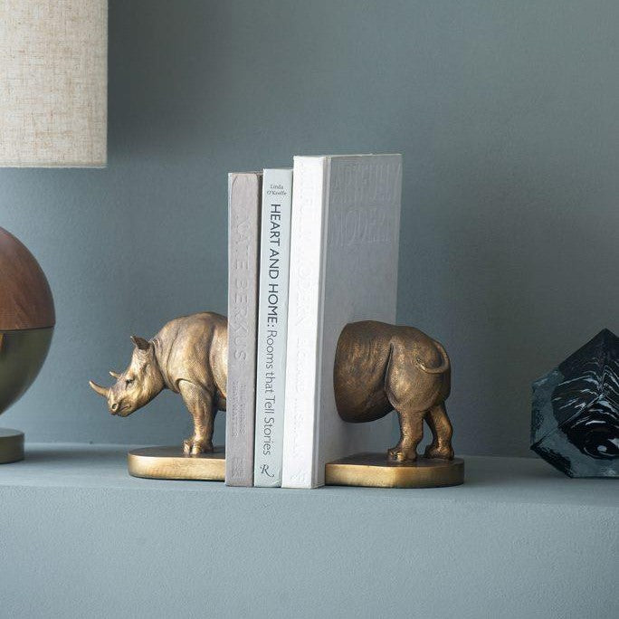 Bronze rhino bookends with books on a shelf, beside a lamp.