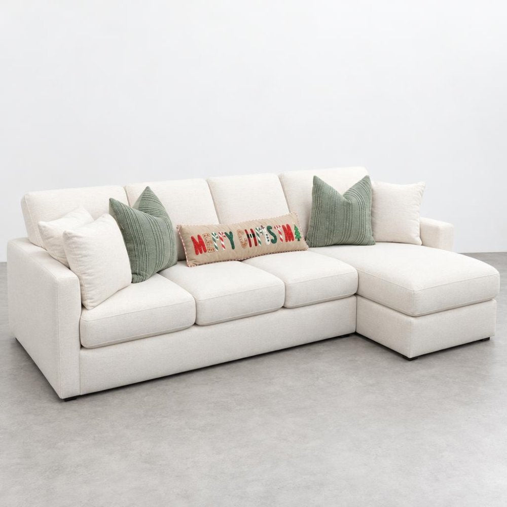 A cream sectional sofa with green cushions and a festive “Merry Christmas” pillow.