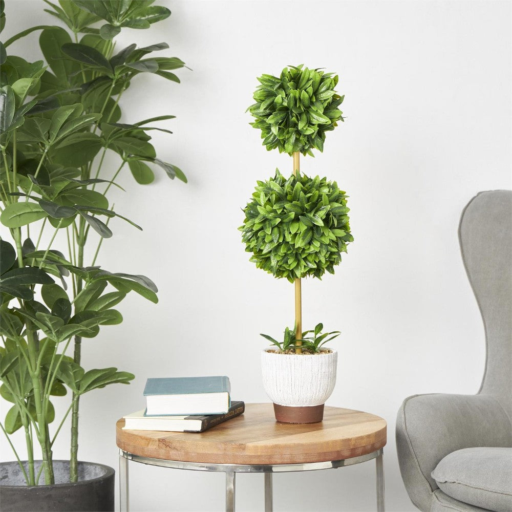 Topiary plant on a round table beside books and a gray chair.