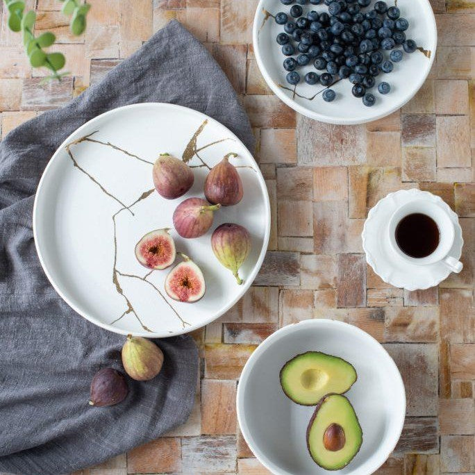 Figs, avocado, blueberries, and coffee on a textured table with a gray cloth.