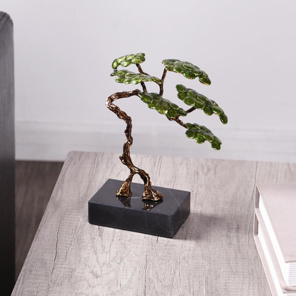 Bronze tree sculpture with green leaves on a wooden table.