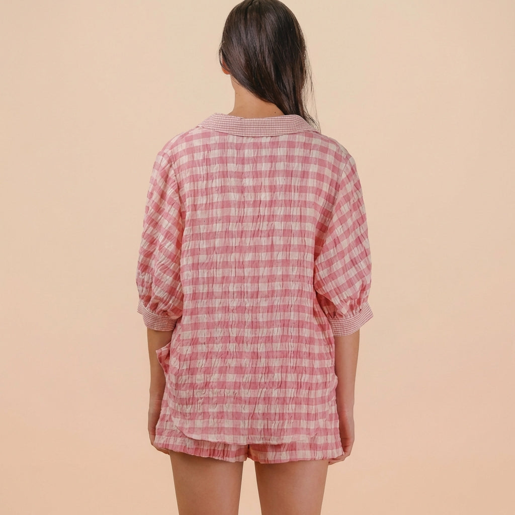 Person in pink checkered outfit standing against a beige background, seen from behind.