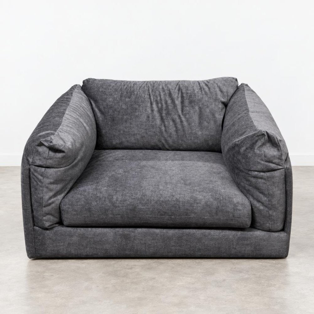 A gray, plush armchair on a plain floor.