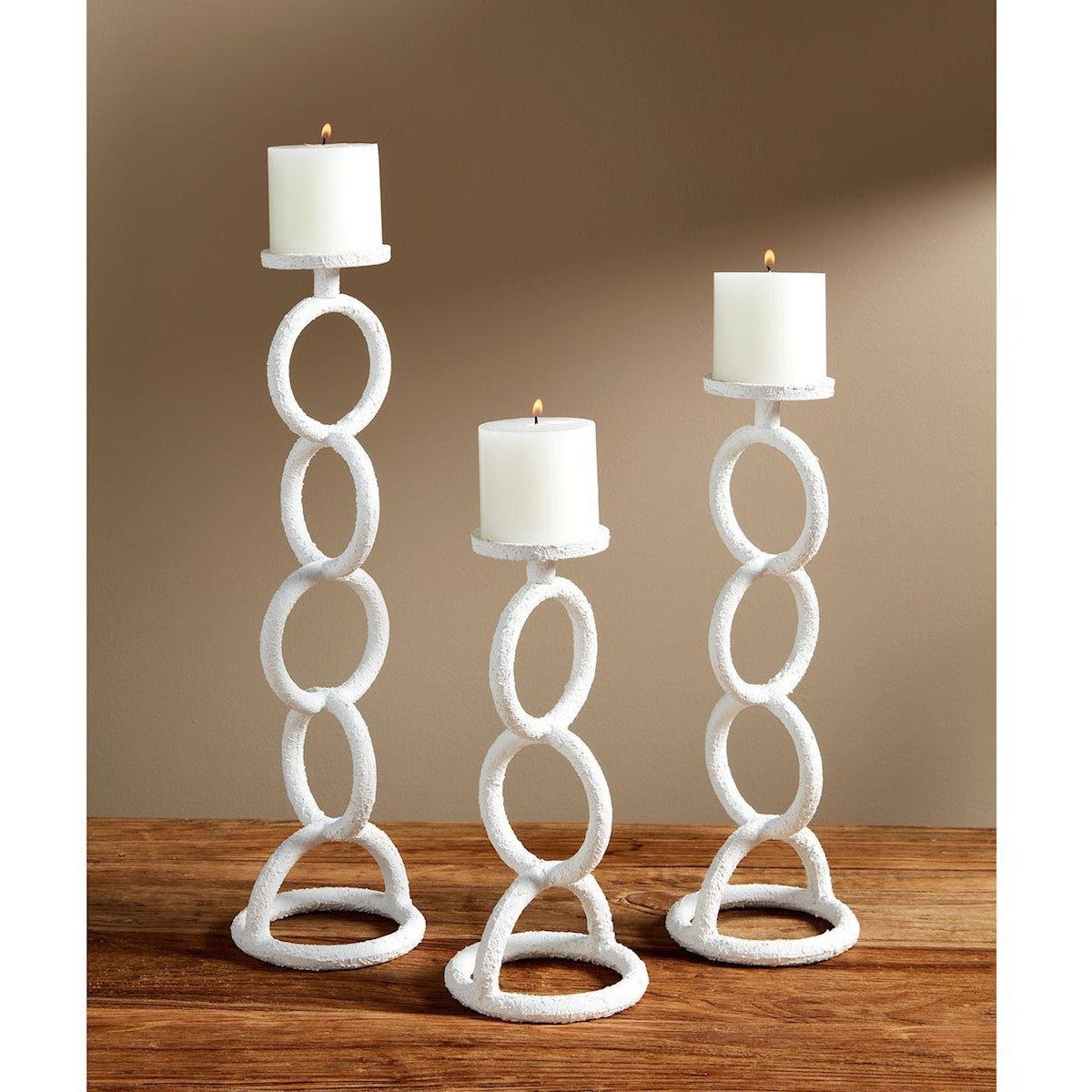 Three white, modern candle holders with lit candles on a wooden table.