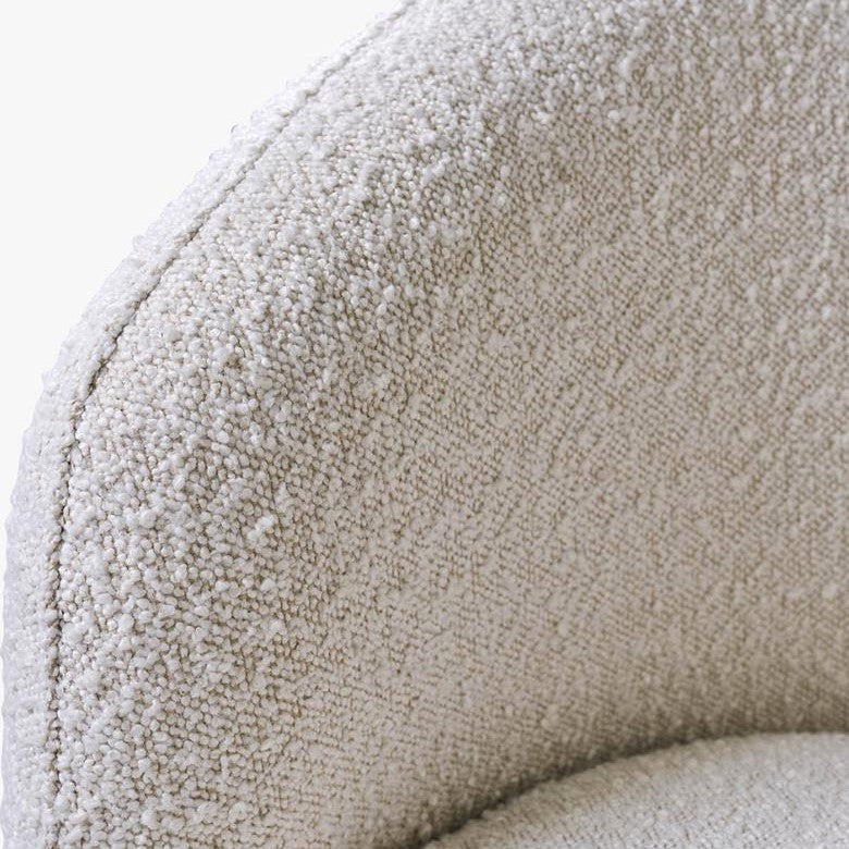 Close-up of a textured, cream boucle fabric on a chair's armrest.