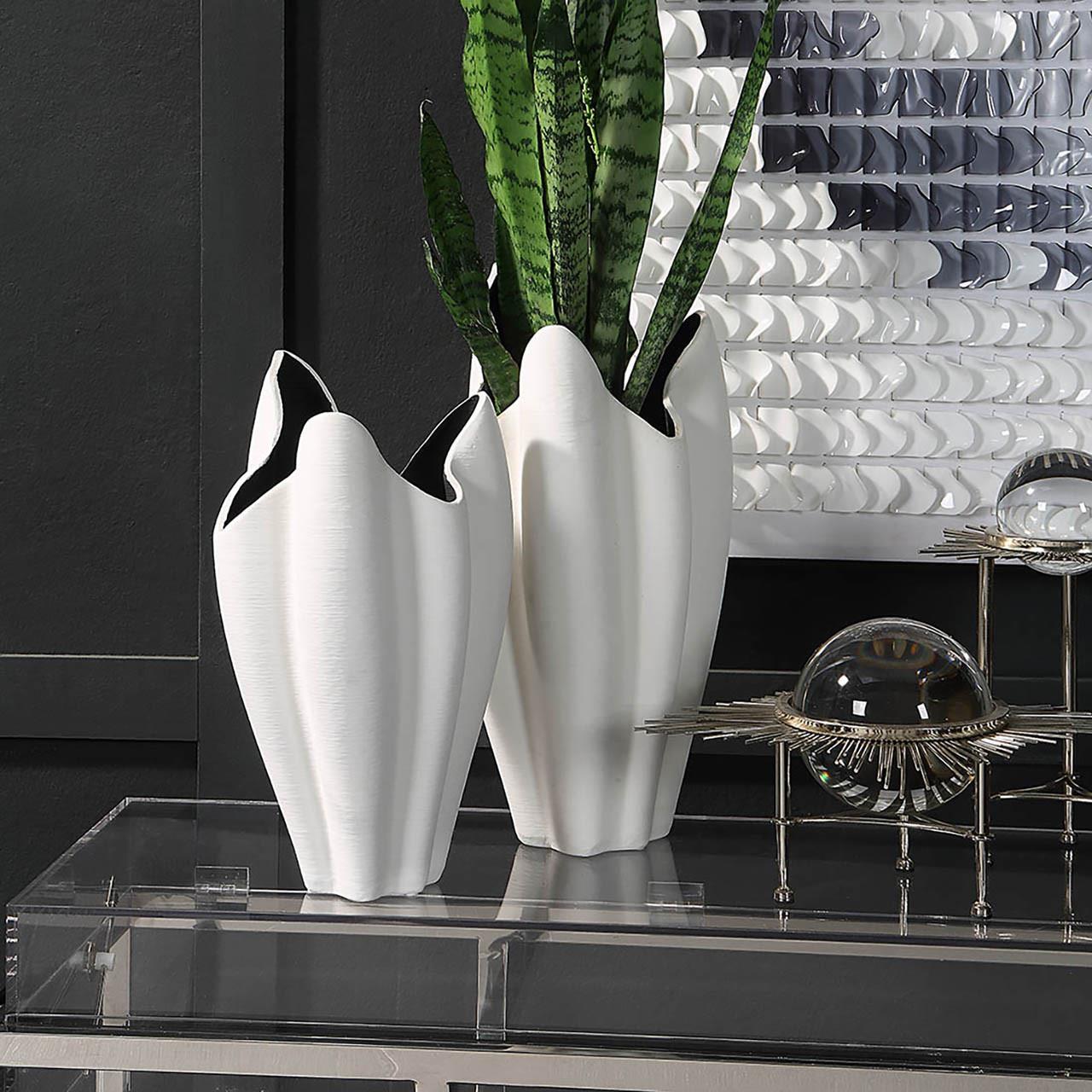 Two elegant white vases with green leaves on a modern decor table.