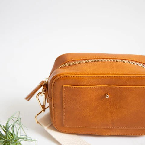 Brown leather bag with a gold zipper, plant on the side.