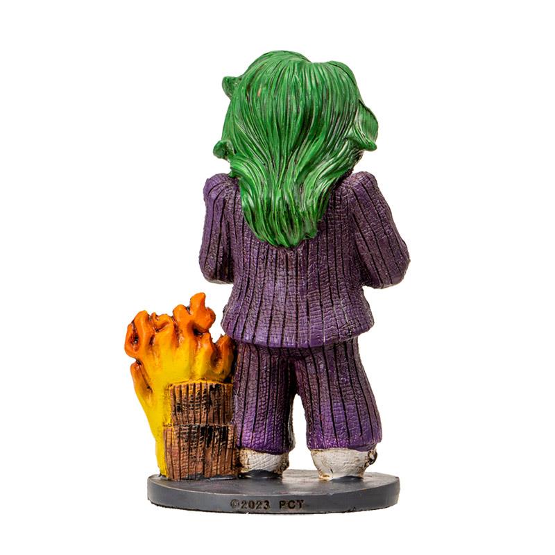 Figurine with green hair, purple suit, next to blazing fire, seen from behind.
