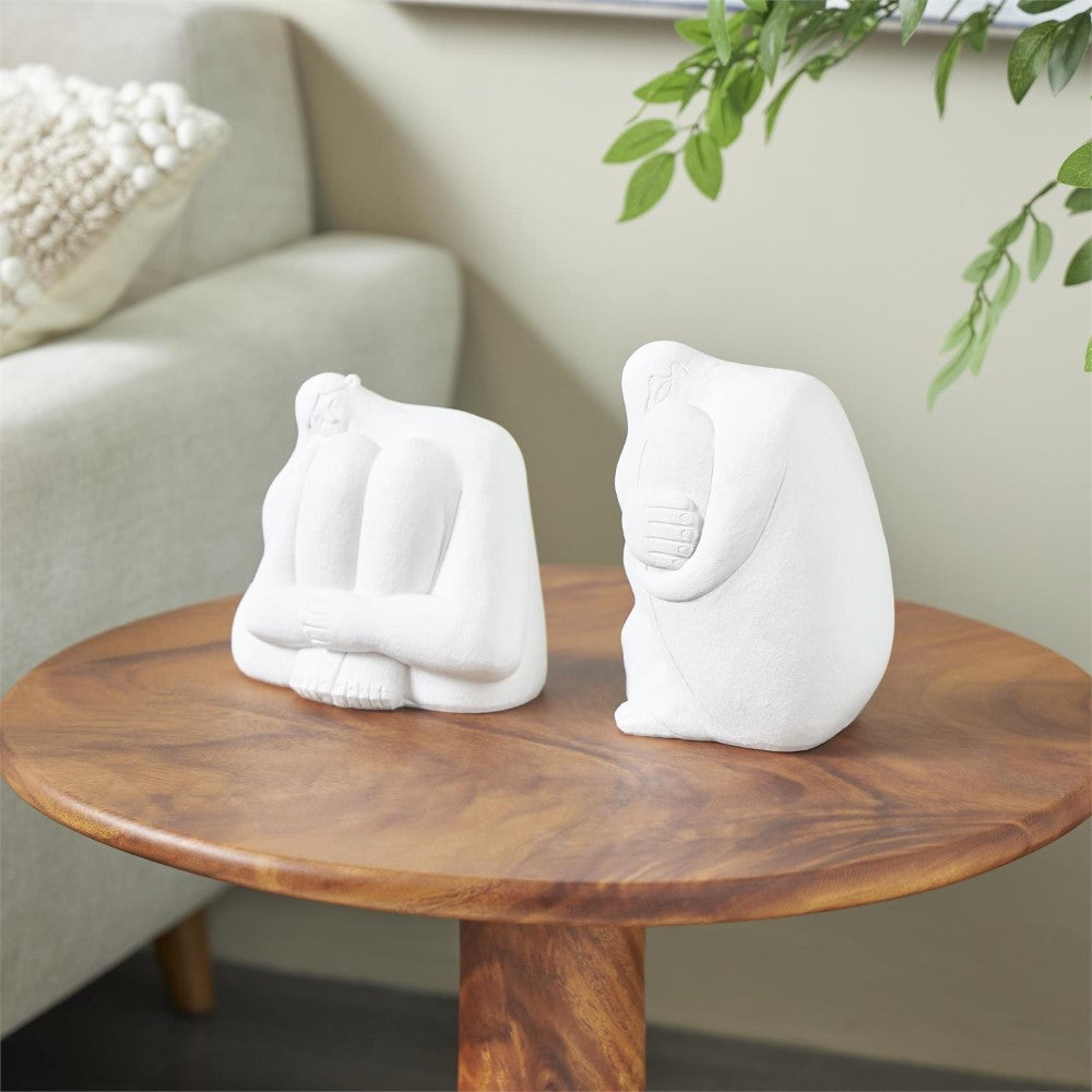 Two white abstract sculptures on a wooden table.