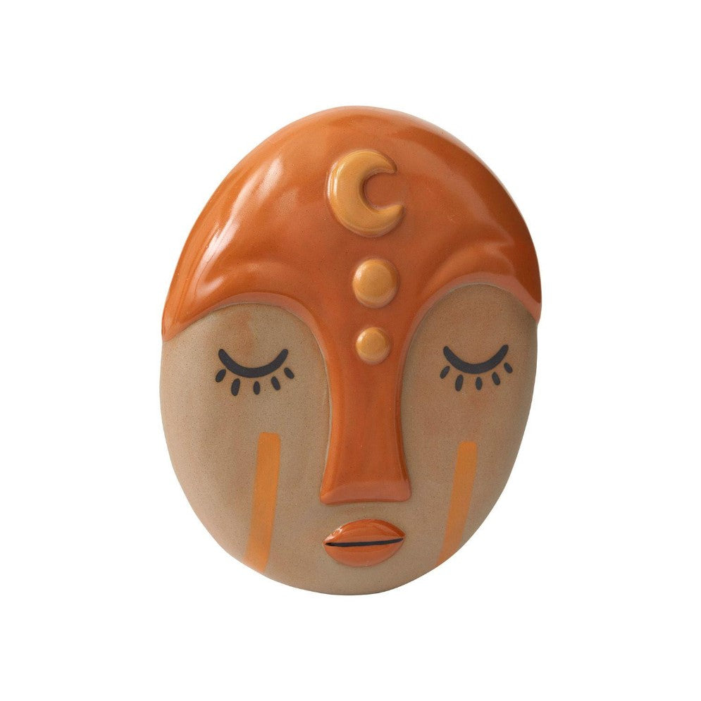 Ceramic face mask with orange details and closed eyes.