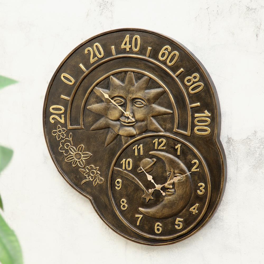 Bronze sun and moon clock with thermometer on a textured wall.