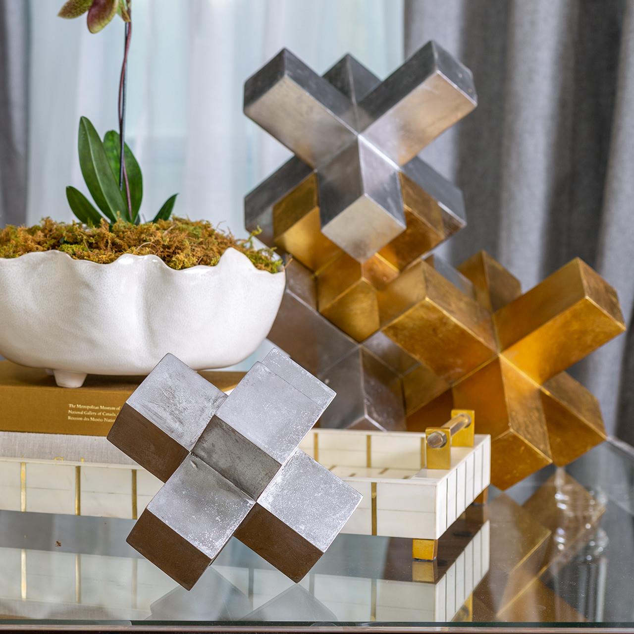 Metallic X sculptures with a decorative plant on a glass table.