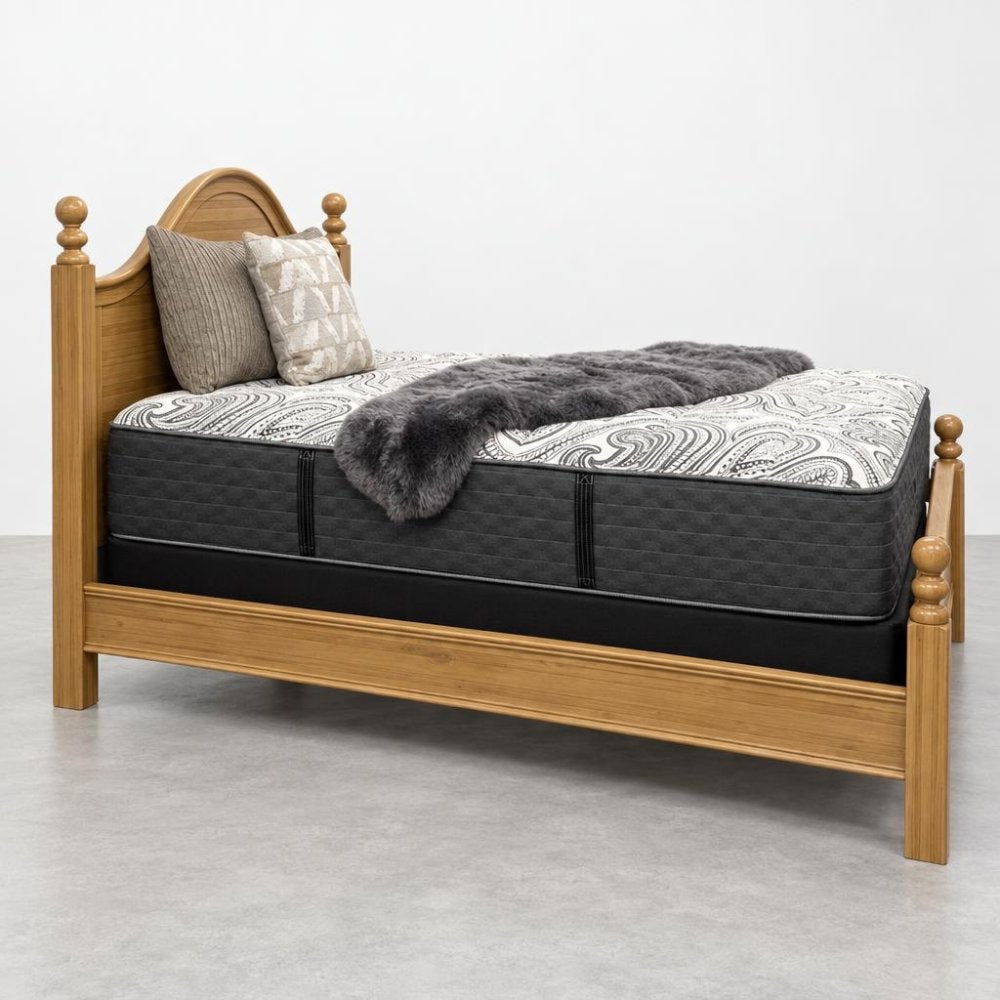 Wooden bed with patterned mattress, pillows, and a gray throw.