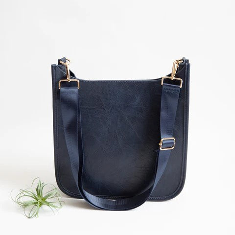 Navy blue shoulder bag with adjustable strap, gold hardware, and a small plant beside it.