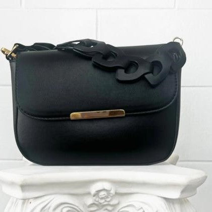 Black leather handbag with chunky strap on ornate white stand.