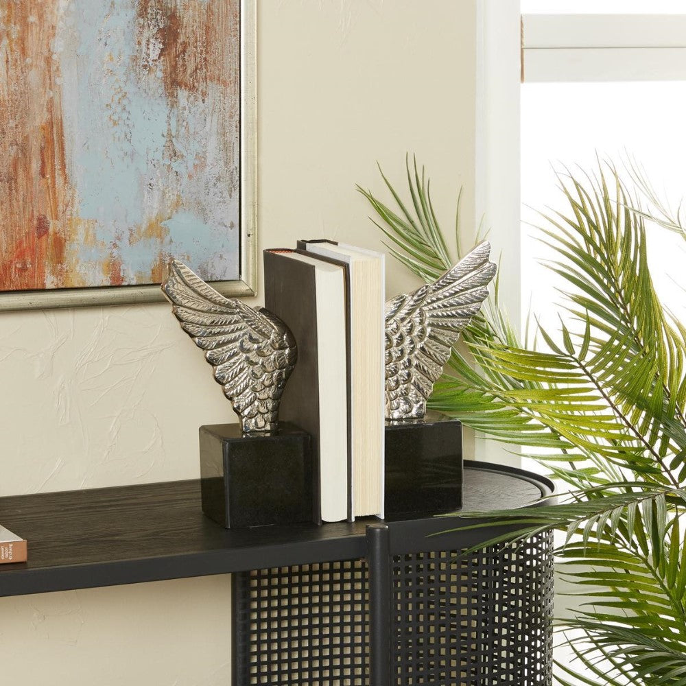 Silver wing bookends holding books on a black shelf near plants.