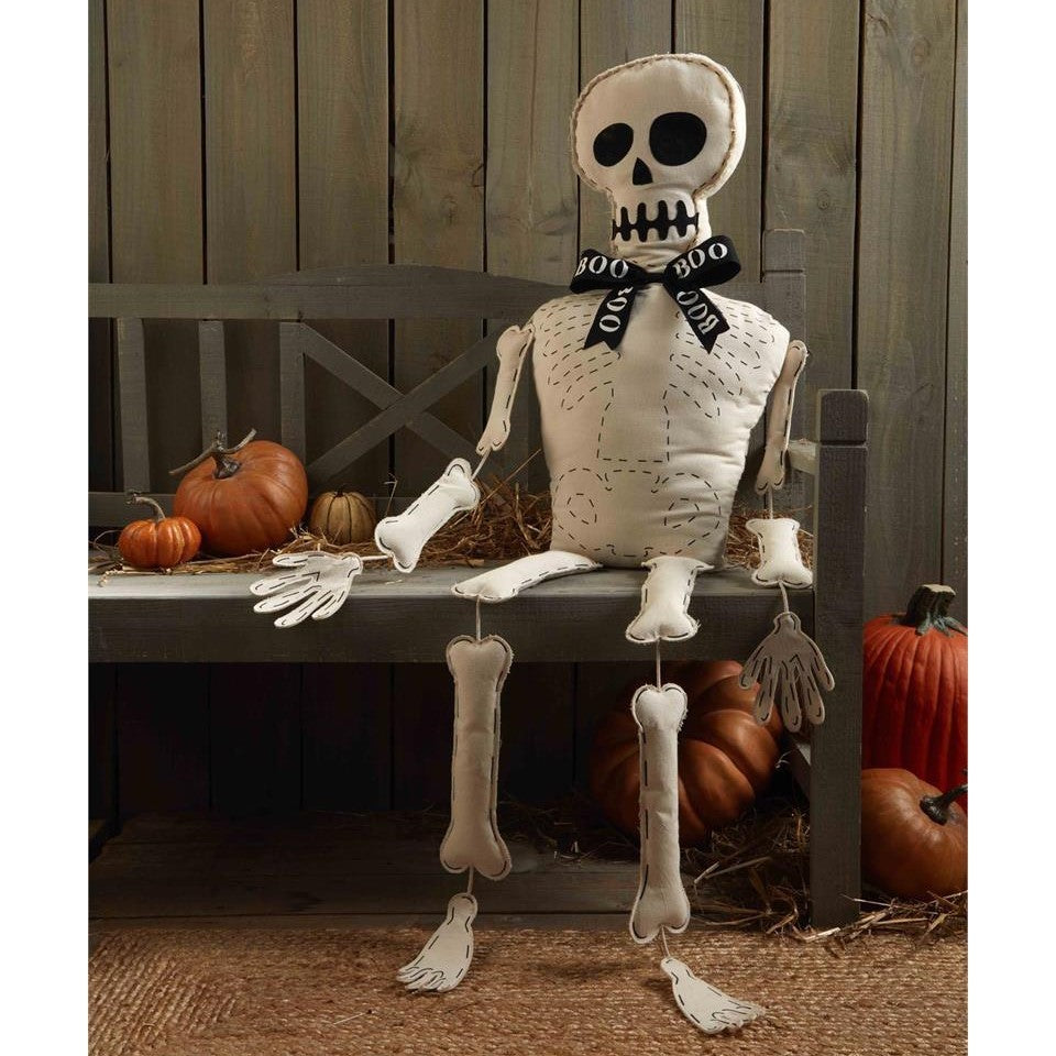 Plush skeleton with "BOO" scarf on bench, surrounded by pumpkins.