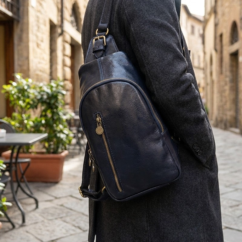 Person in gray coat with navy sling bag in a cobblestone street.