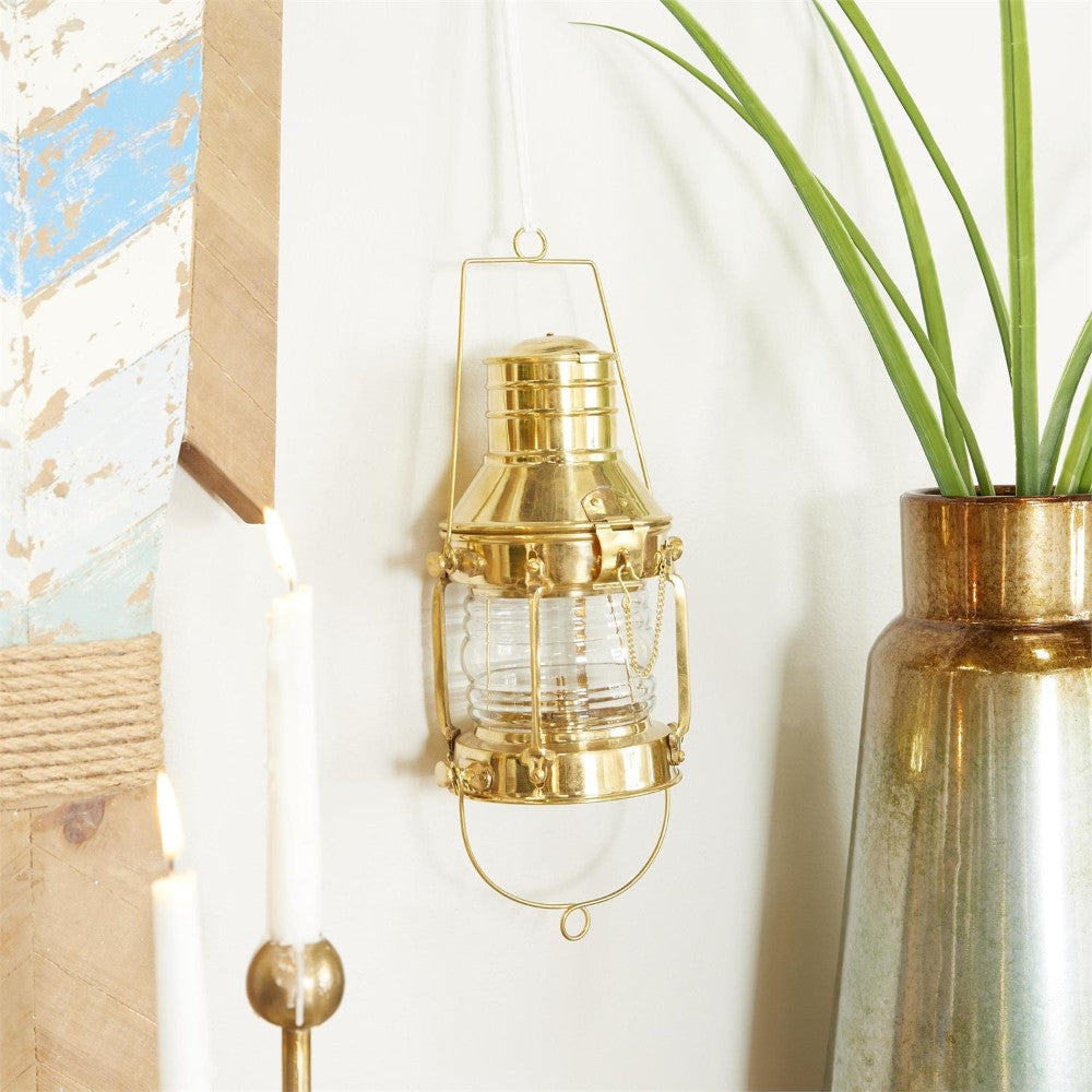 Brass lantern on white wall, with candles and a large vase nearby.
