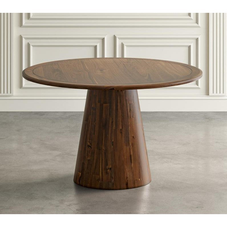 Round wooden table with a tapered base, set against a paneled wall.