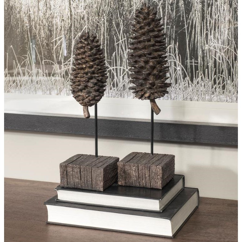 Two decorative pinecones on stands, set on books, with nature art in the background.