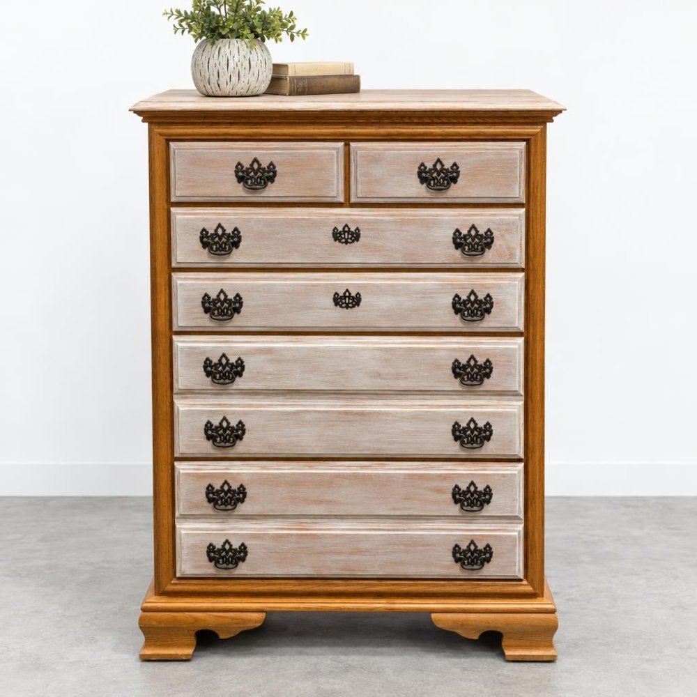 A vintage wooden chest of drawers with ornate dark pulls, topped with books and a leafy plant.