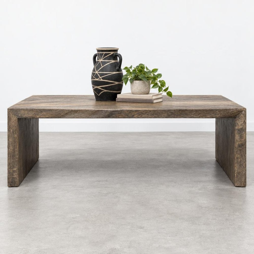 Wooden table with a vase, plant, and books on a minimalistic backdrop.