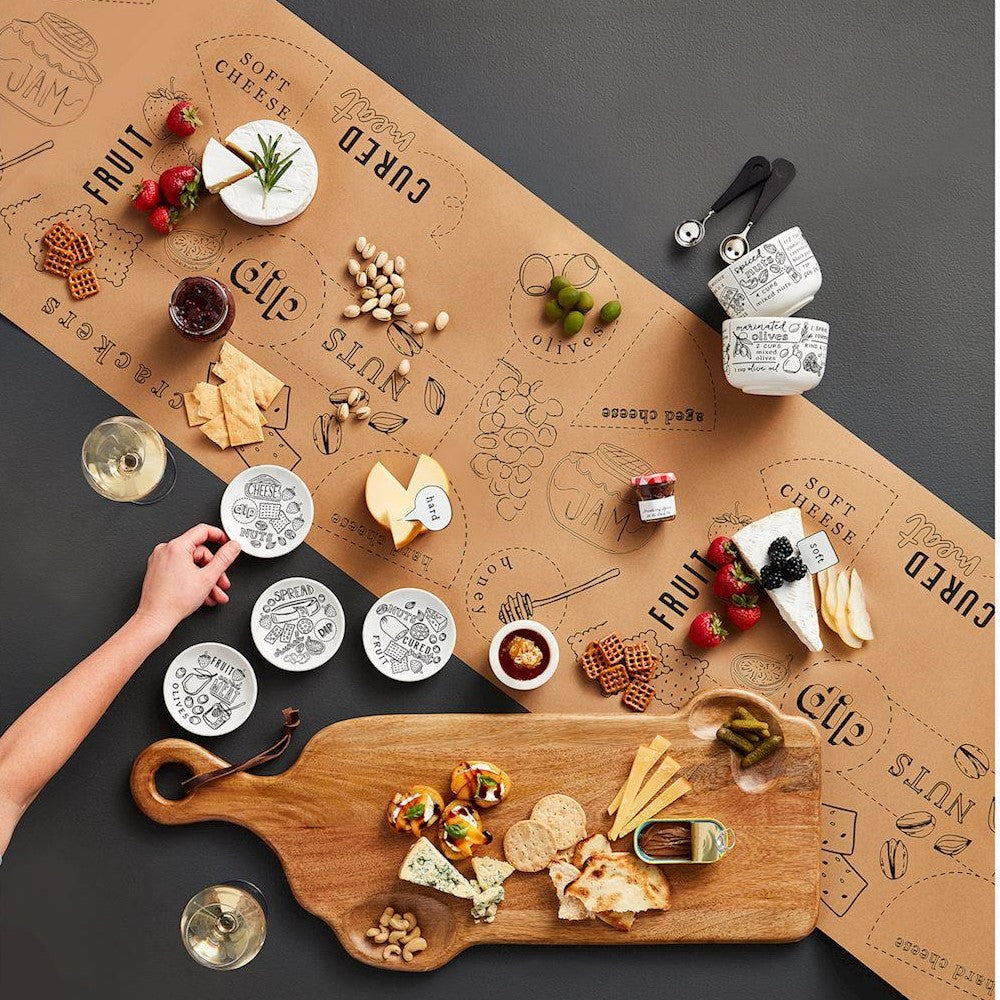 Cheese platter setup with snacks, wine, and labeled placement on paper.