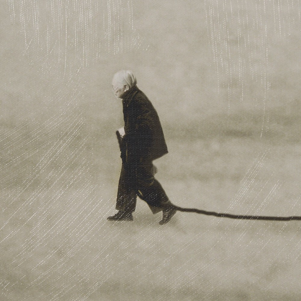 Elderly person walking, pulling a long shadow behind them.