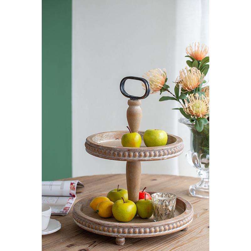 Two-tier wooden fruit stand with apples on a table by flowers.